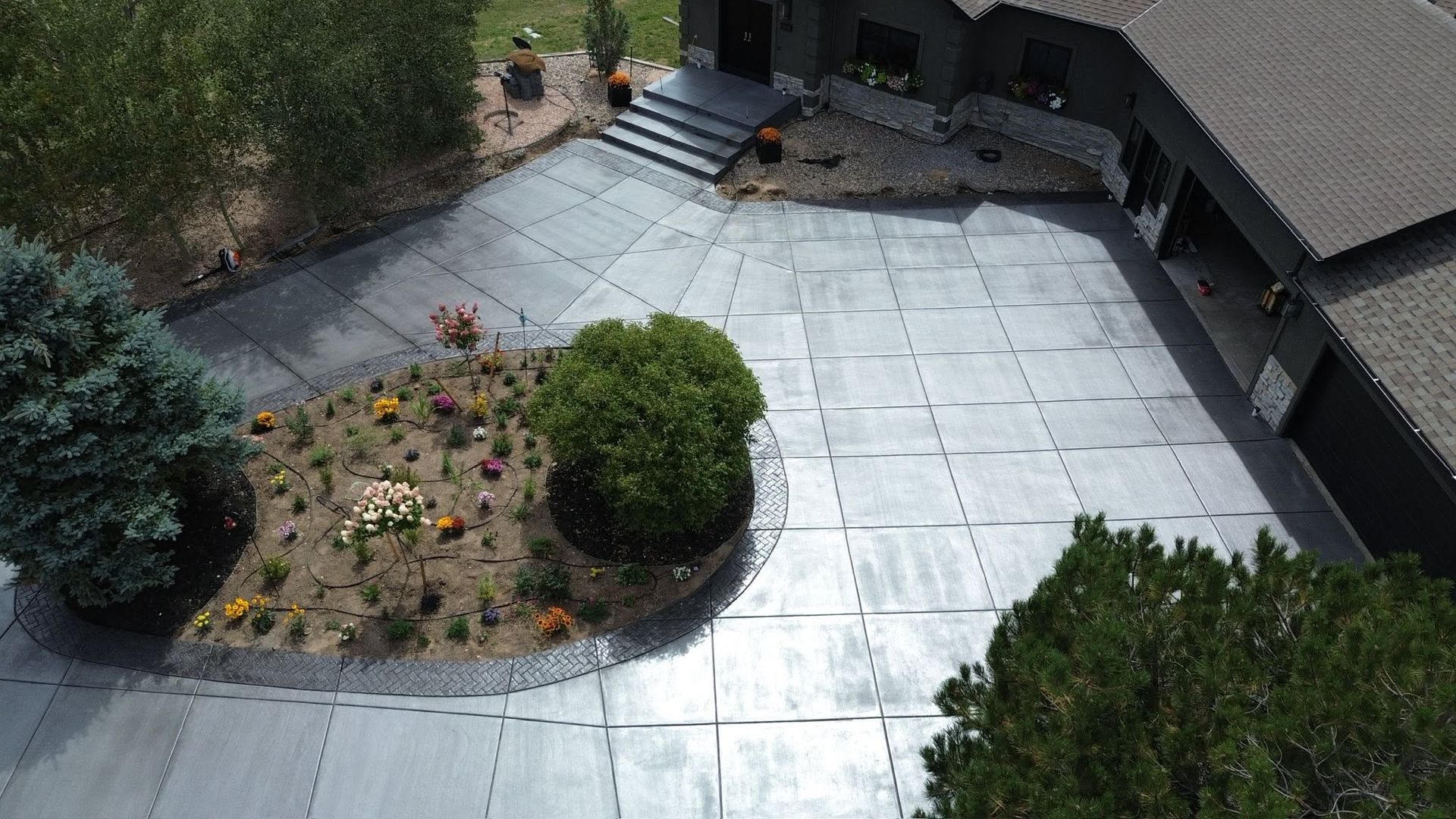 Curved patio with silver tarp, circular flower bed, and outdoor chairs beside a house