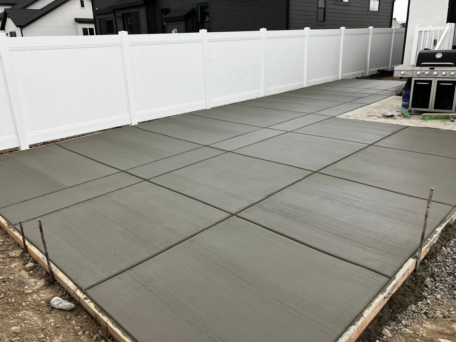 Freshly poured concrete patio beside a white vinyl fence and neighboring houses