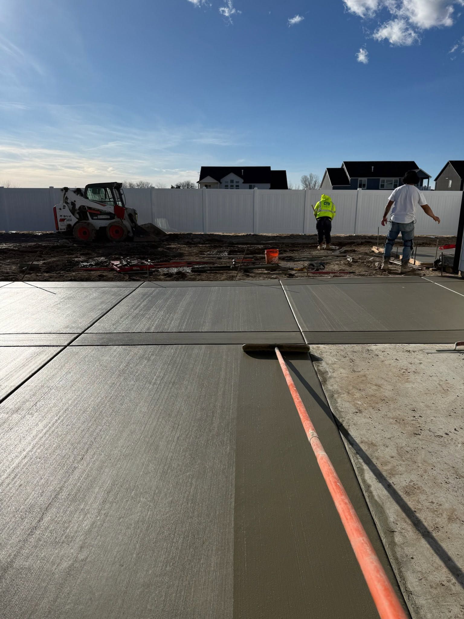 Construction workers inspect a damaged road slab with exposed rebar and a fresh concrete joint.