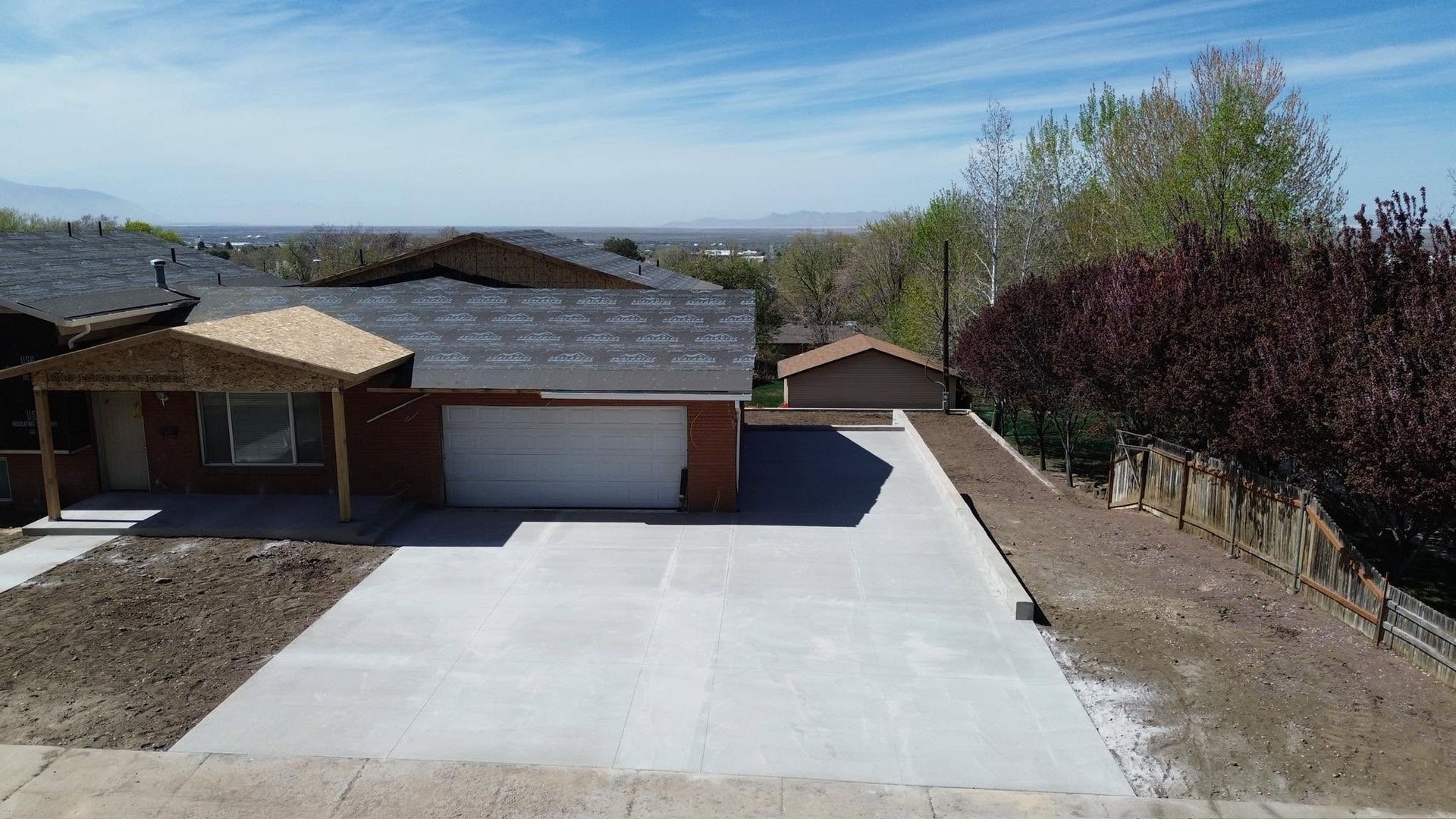 House with a large concrete driveway and garage, viewed from above on a sunny day.