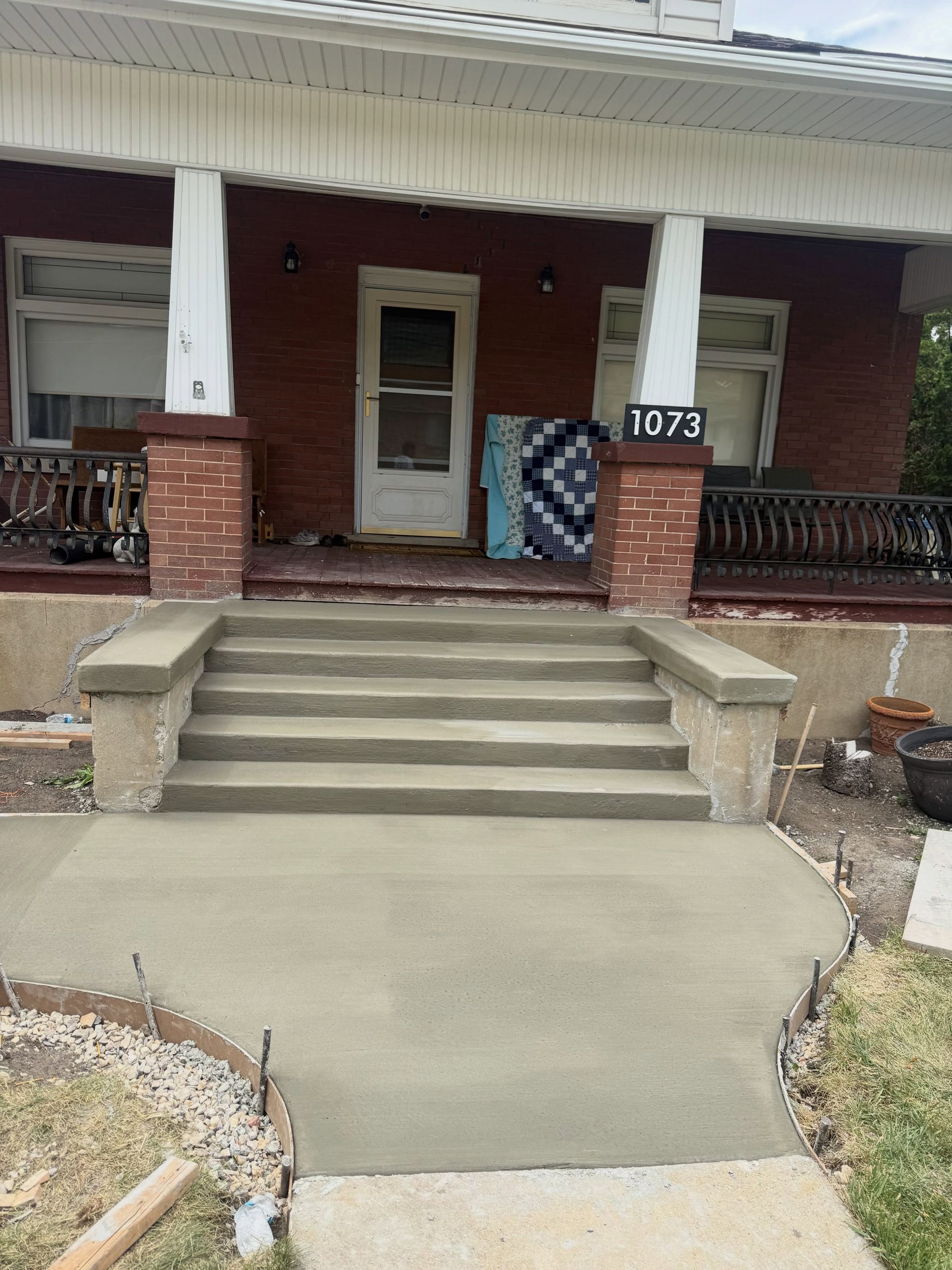 Front porch with stairs, brick columns, and a ramp leading to the entrance of house number 1073.