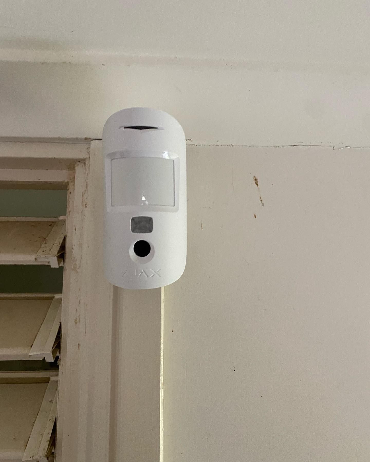 A White Motion Sensor is Mounted on a White Wall Next to a Door — DGC Tech Solutions In Northern Beaches, QLD