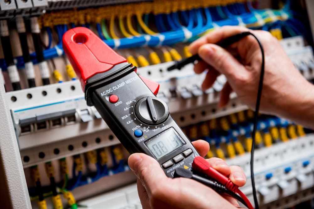A Person is Holding a Clamp Meter in Front of an Electrical Cabinet — DGC Tech Solutions In Mareeba, QLD