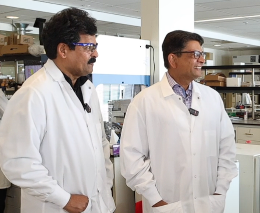 Two men in lab coats smile in a lab.