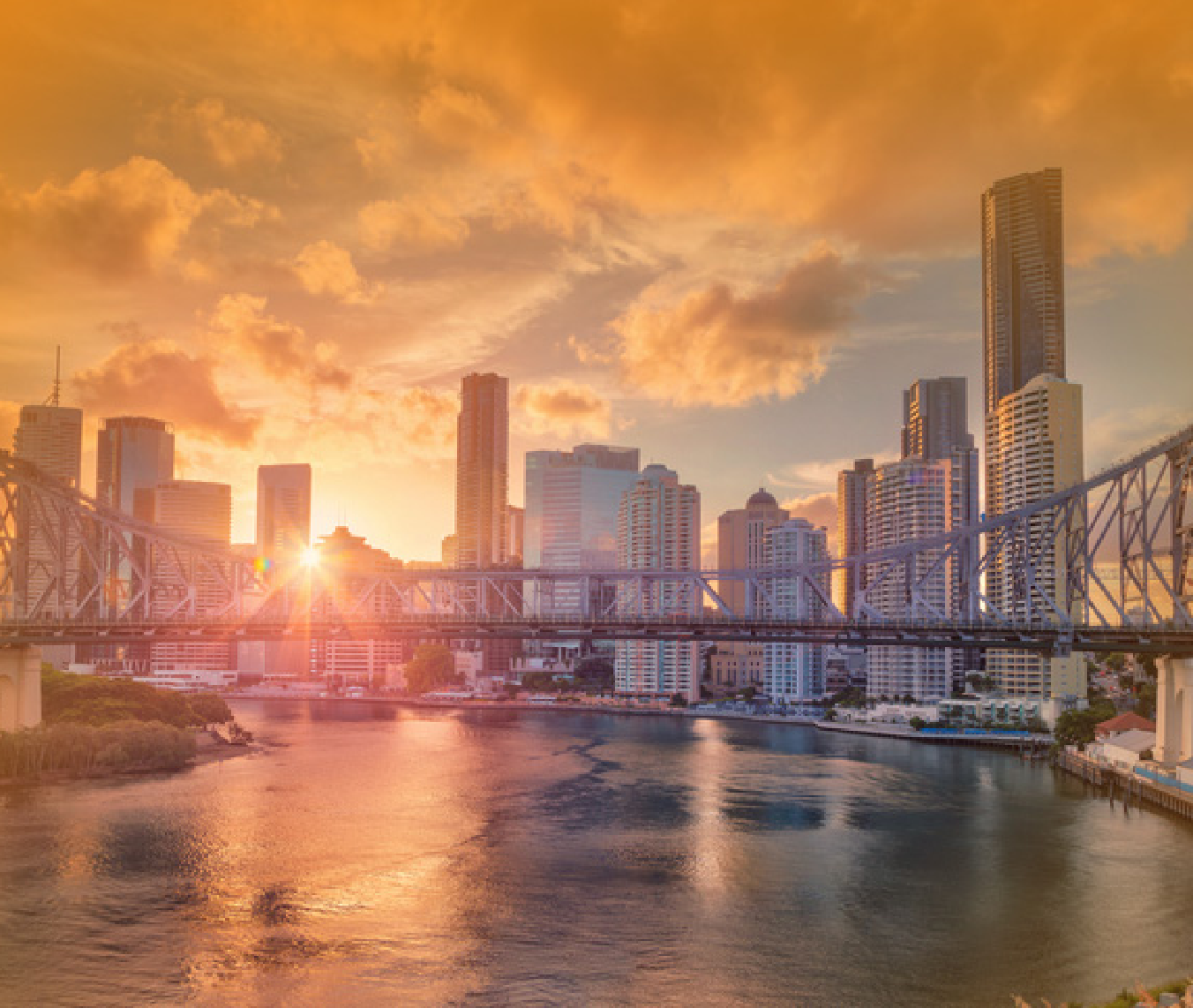 A city skyline with a bridge over a river at sunset.