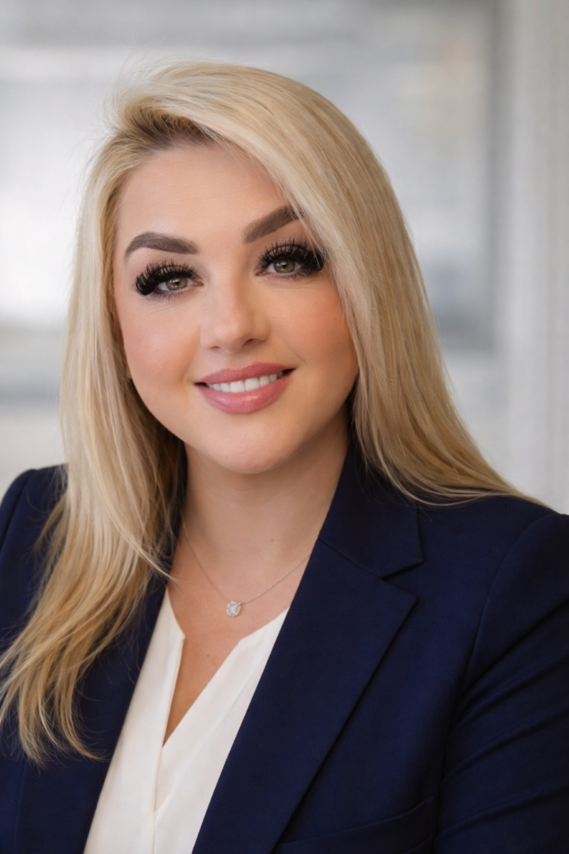 Smiling woman with long blonde hair in a navy blazer against a blurred indoor background