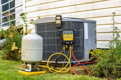 HVAC technician working on an air conditioning unit outside, gauges and hoses connected.