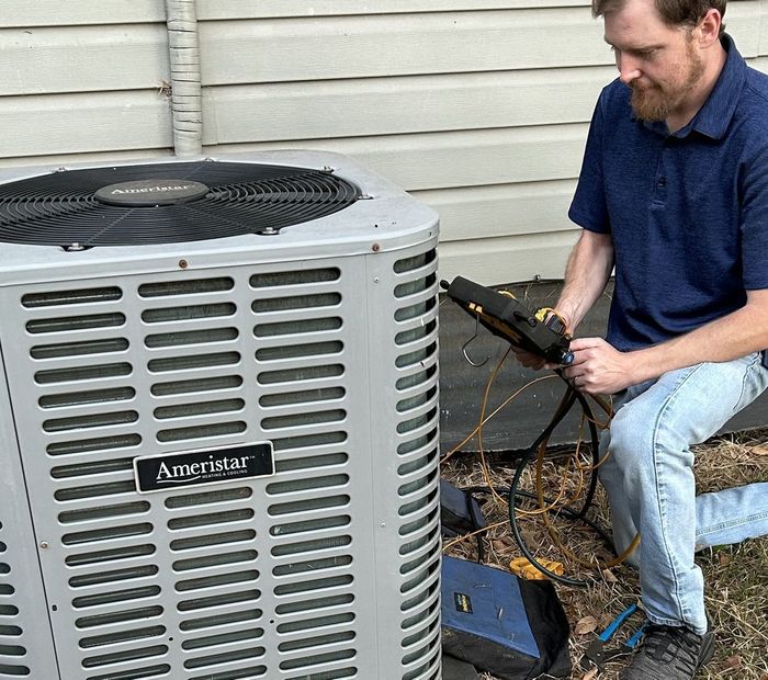 Technician checking wiring on an outdoor air conditioner unit beside a house