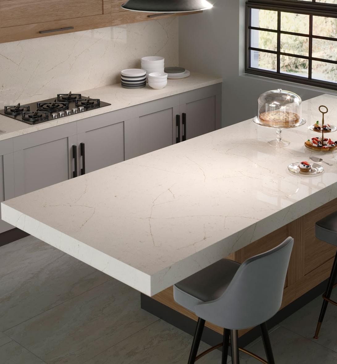Modern kitchen with light countertops, gray cabinets, and a countertop island with bar stools.