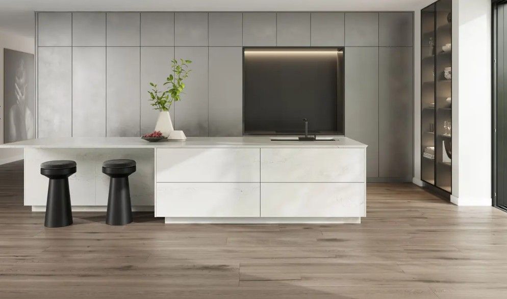 Modern kitchen with a large island and gray cabinets, wooden floor, black stools.
