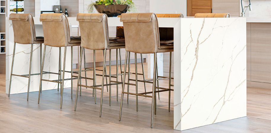 Kitchen island with marble-like finish, four beige leather bar stools, and a bowl of greenery.