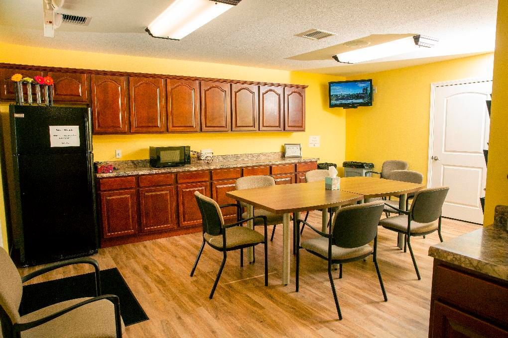Kitchen with wood cabinets, black fridge, dining table, chairs, and wall-mounted TV under fluorescent lights