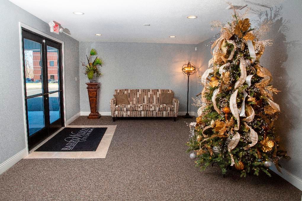 Lobby with a decorated Christmas tree, bench, potted plant, and glass doors on a carpeted floor.