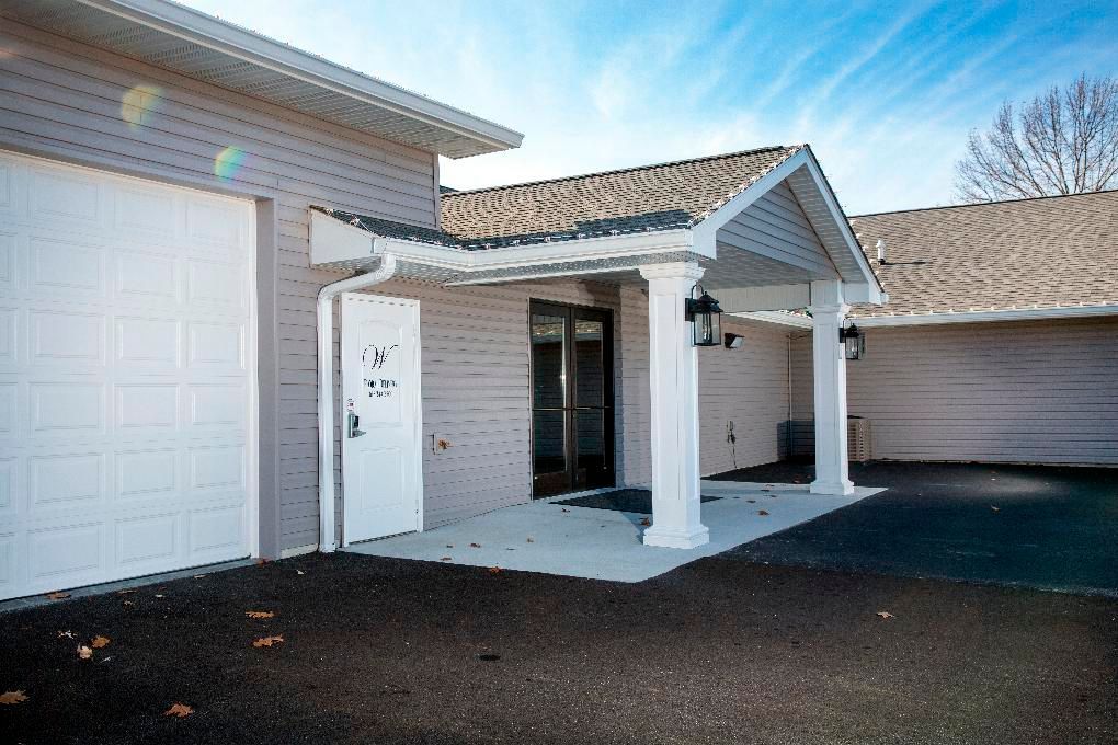Front entrance of a house with a covered porch, garage door, and dark driveway under a blue sky