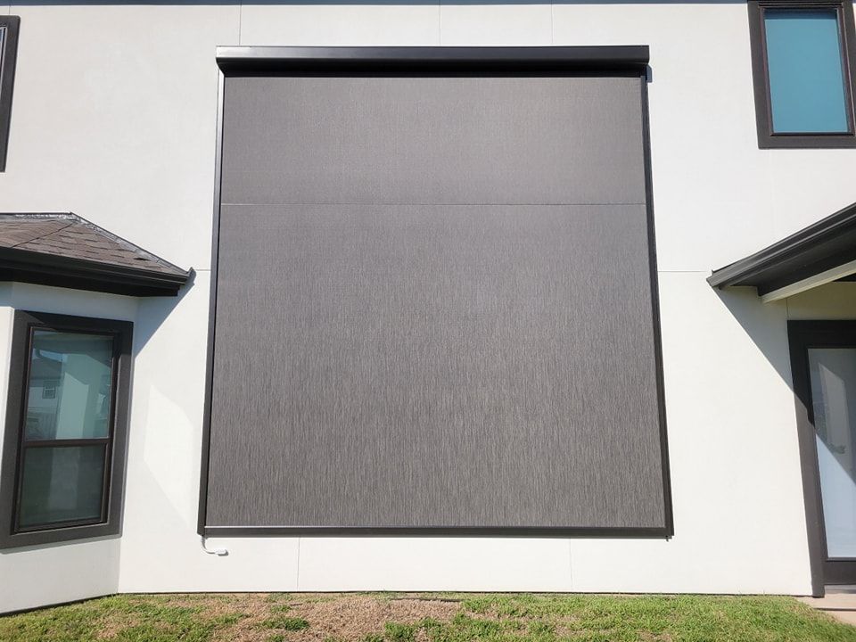 A large window with a blind on it is on the side of a house.