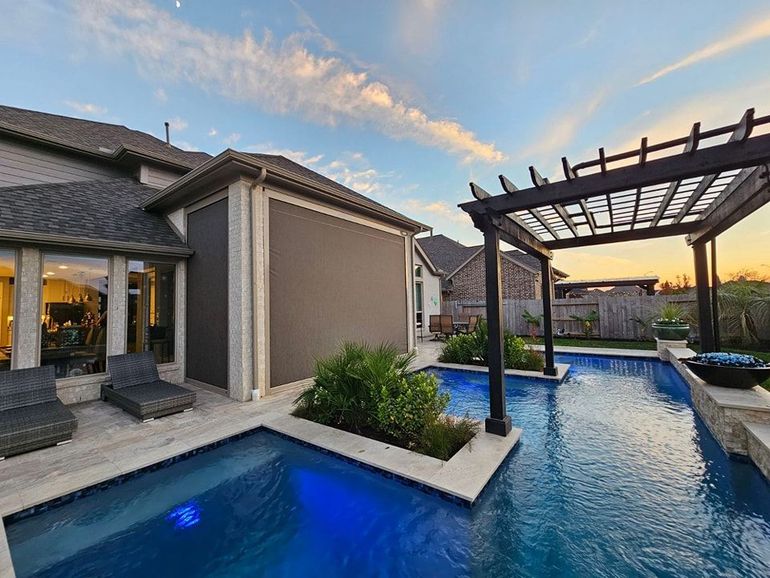 A large swimming pool with a electric shades for patio in the backyard of a house in texas.