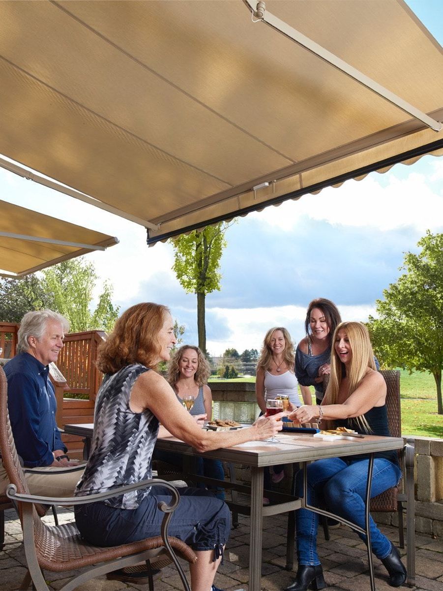 A happy group of people are sitting at a table under a motorized awning in texas.