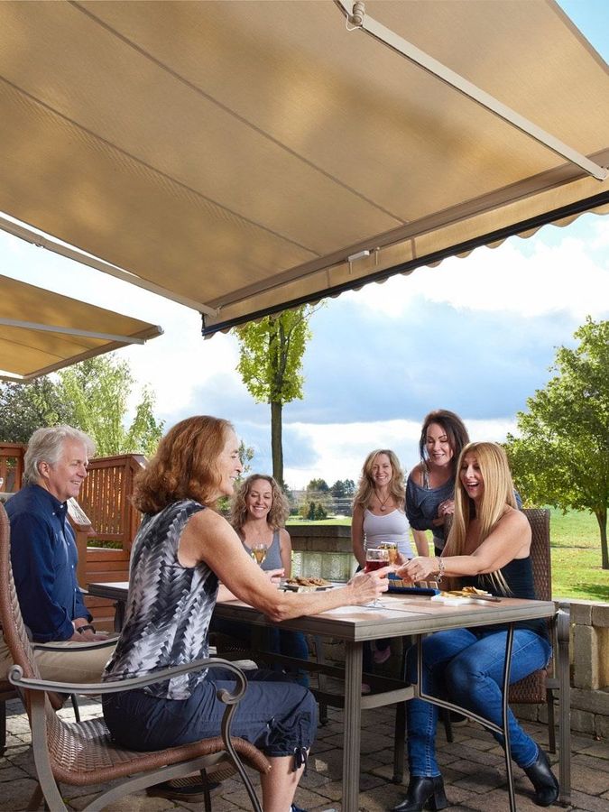A happy group of people are sitting at a table under a motorized awning in texas.