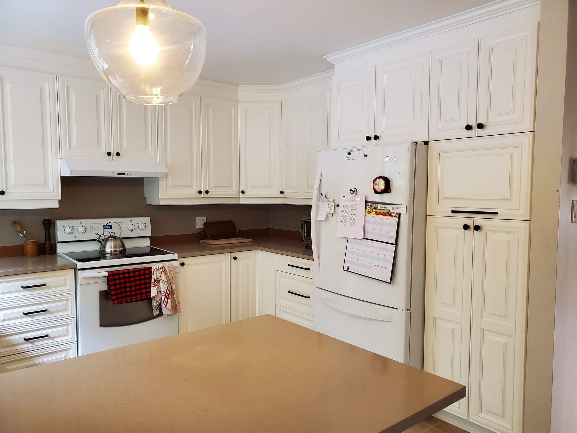 Une cuisine avec des armoires blanches, une cuisinière, un réfrigérateur et une table.