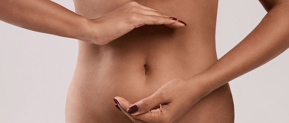 Torso di una persona che misura la vita con le mani, su sfondo neutro.