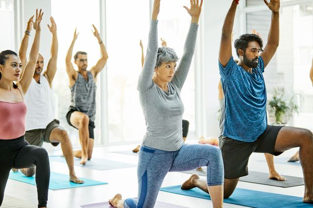 Persone che praticano stretching yoga in uno studio luminoso, inginocchiate con le braccia sollevate sui tappetini.