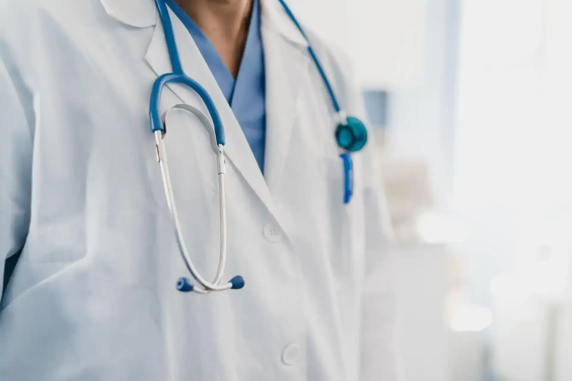Medico in camice bianco con stetoscopio blu al collo, primo piano ravvicinato.