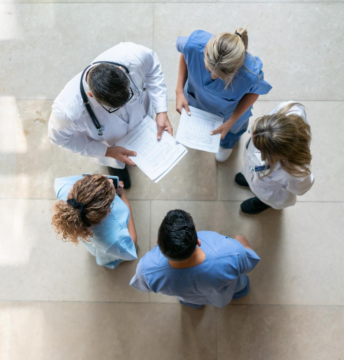Vista dall'alto di quattro persone in camice medico che discutono di documenti in un corridoio luminoso.