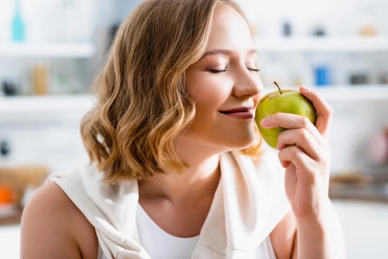 Una donna annusa una mela verde in una cucina luminosa.