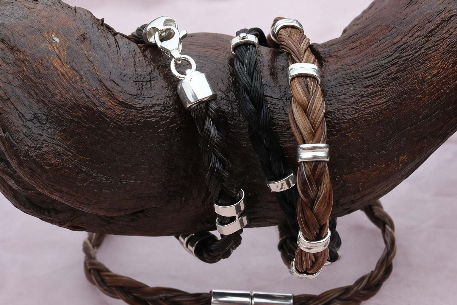 Deux bracelets tressés en cuir, l’un noir et l’autre marron, fermés autour d’une surface en bois foncé.