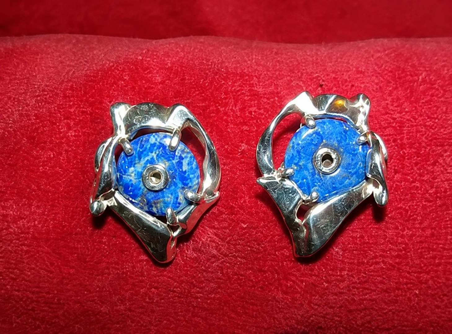 Deux boucles d’oreilles florales bleues et argentées sur un fond en tissu rouge