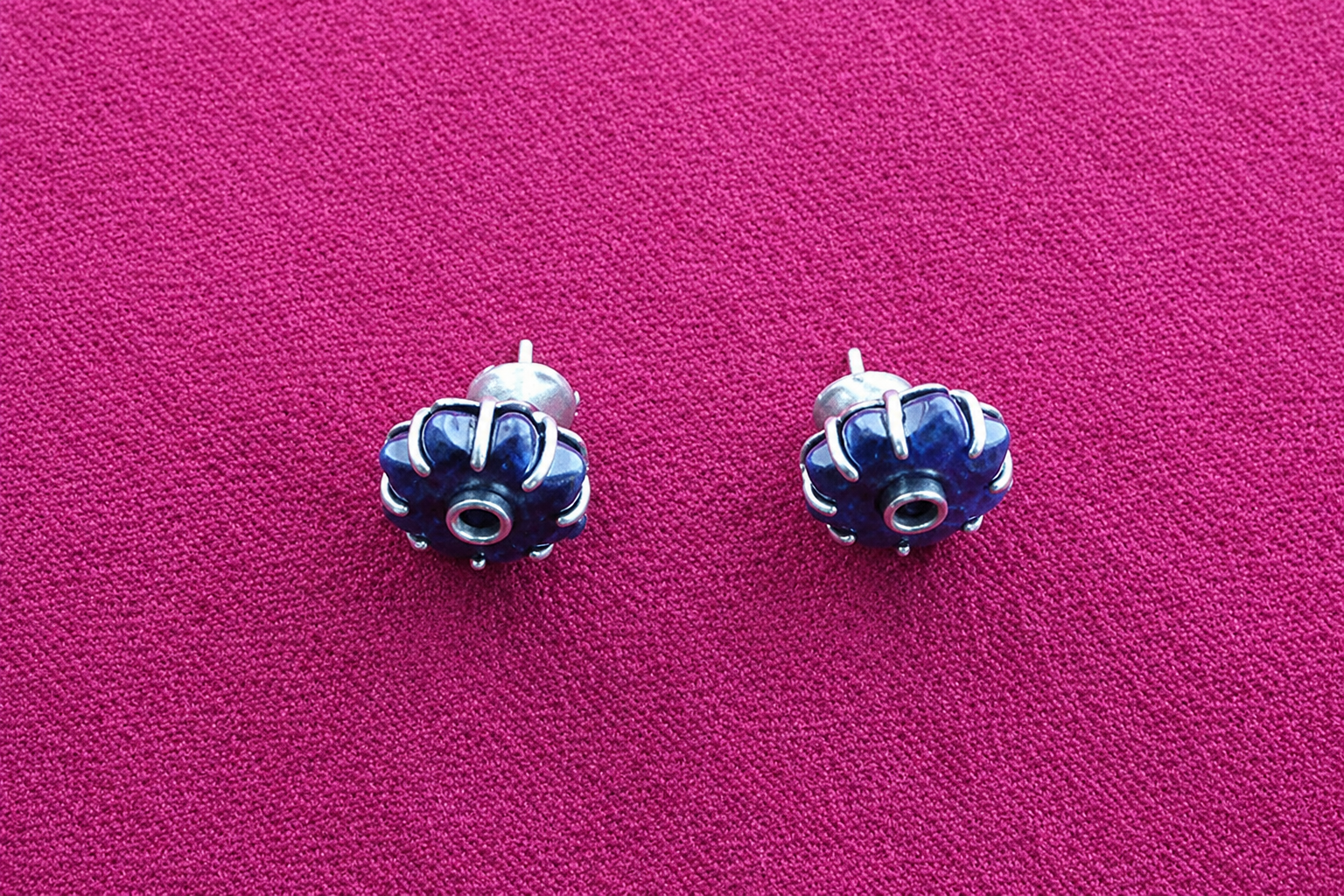 Deux petites boucles d’oreilles bleues ornées de pierres sur un fond en tissu rose