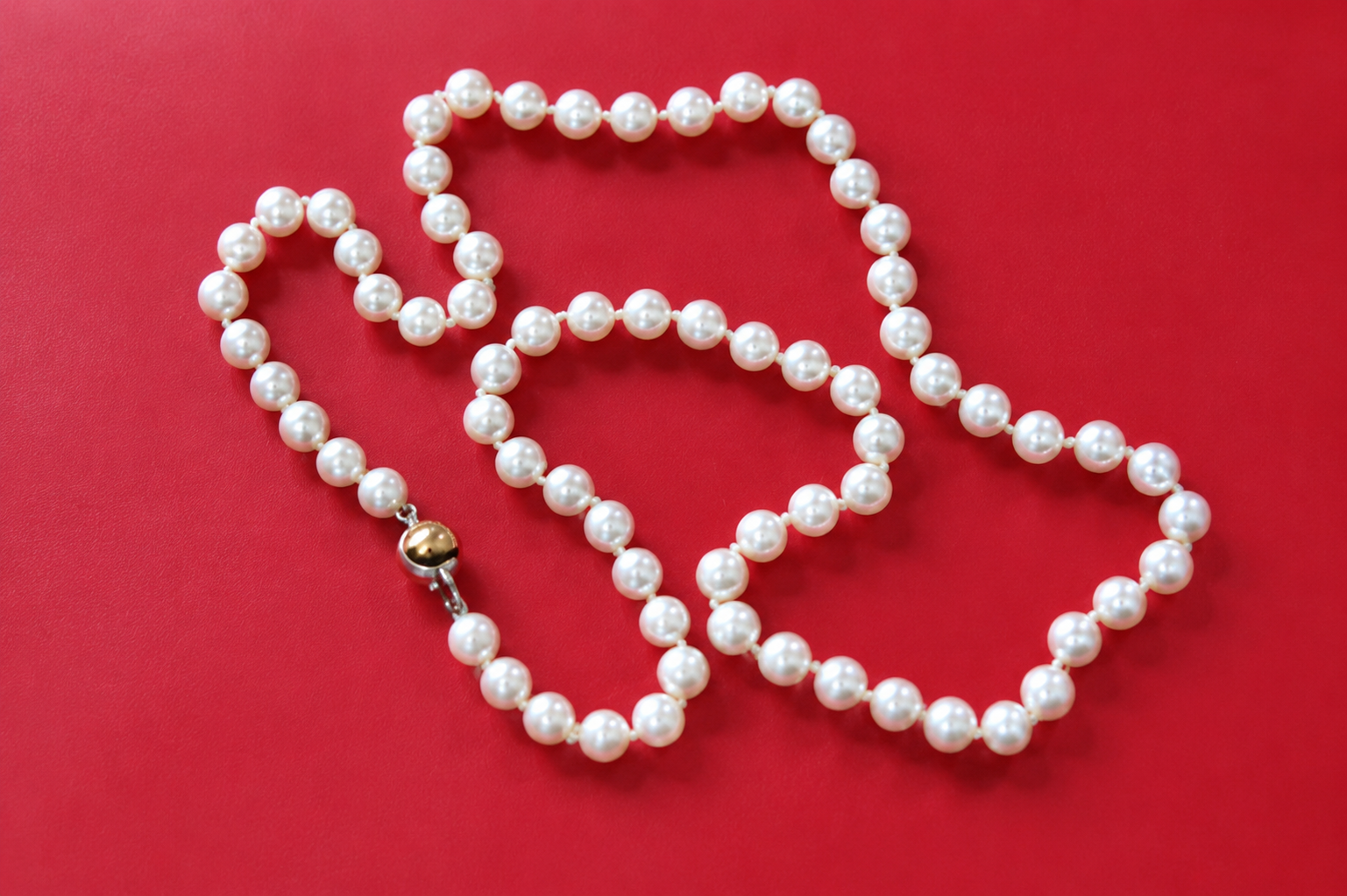 Collier de perles avec fermoir en or disposé en forme de cœur sur fond rouge