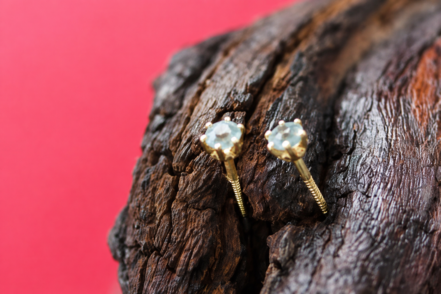 Deux petites boucles d’oreilles en forme d’étoile sur du bois foncé, sur fond rose