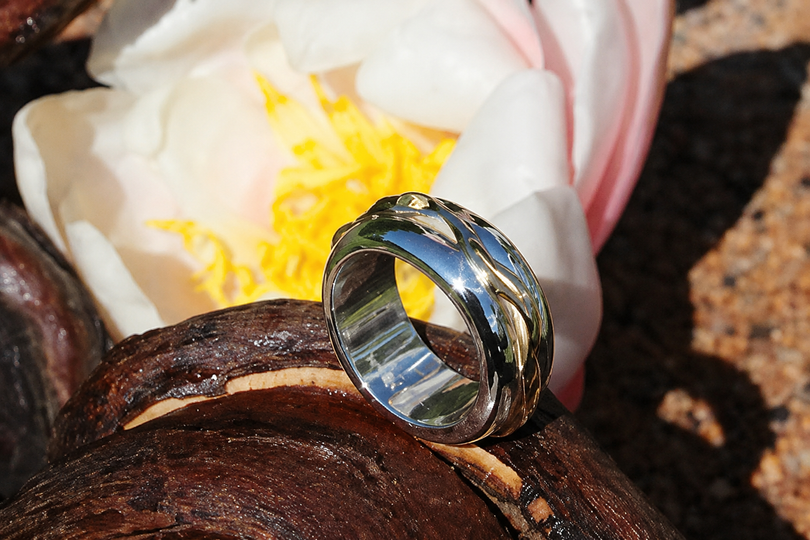 Bague en métal trois tons posée sur une branche en bois, à côté d’une fleur blanche au cœur jaune