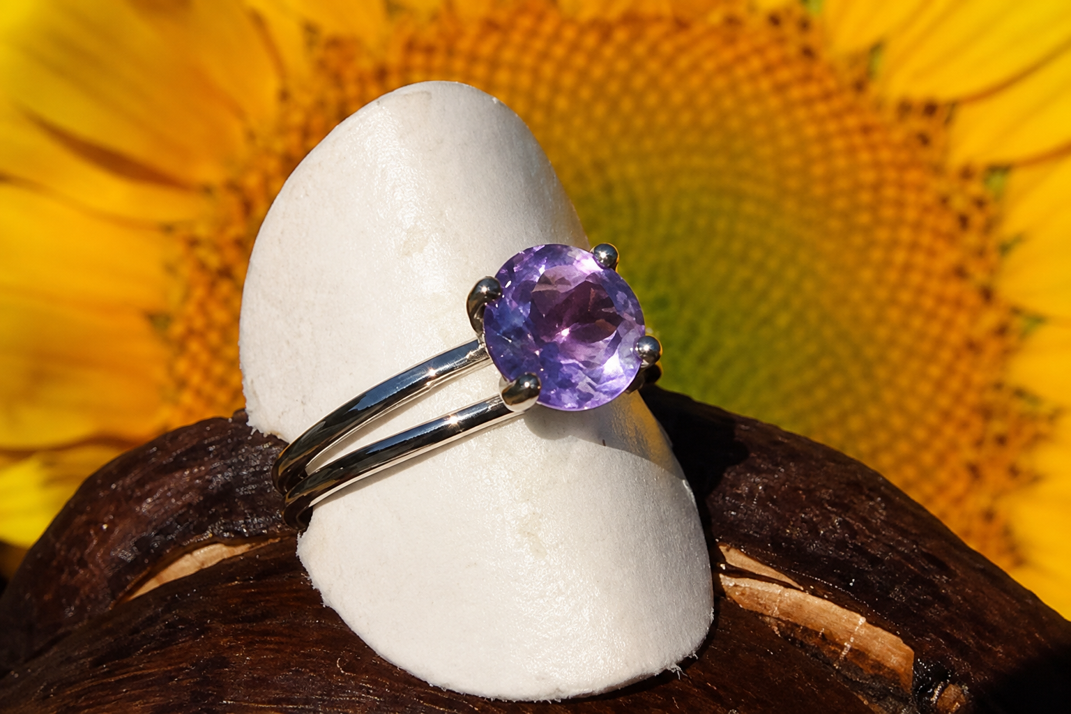 Bague en argent ornée d’une pierre précieuse violette, posée sur un présentoir blanc devant un fond de tournesols