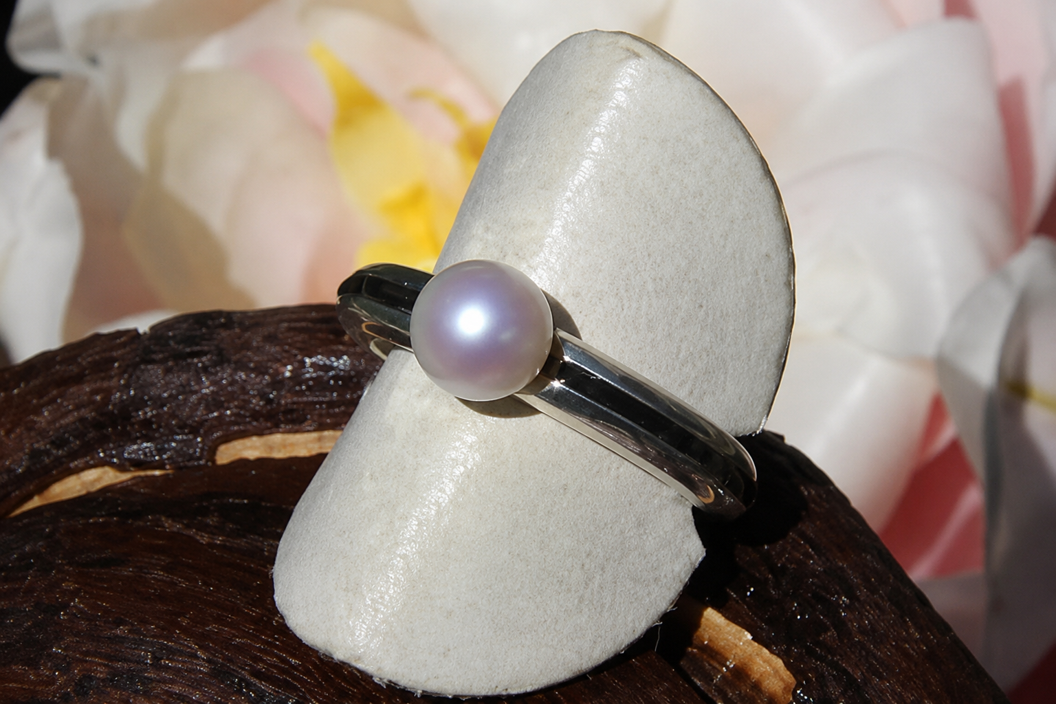 Bague en perles sur un présentoir blanc, avec des fleurs floues en arrière-plan