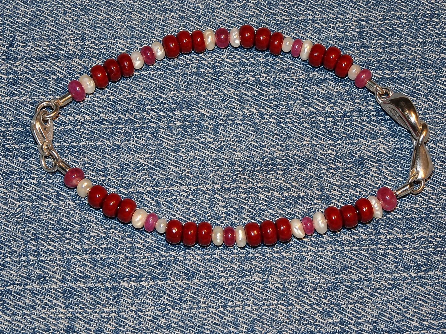 Bracelet rouge à perles avec fermoirs argentés posé sur un tissu en denim bleu.