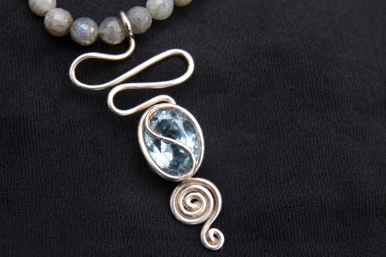 Collier pendentif en spirale argentée avec des pierres bleues ovales sur fond noir