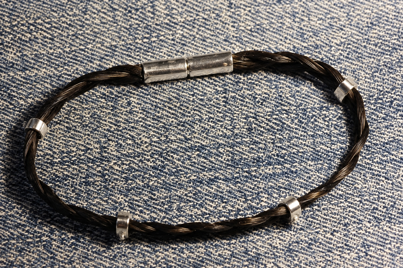 Bracelet tressé noir avec fermoirs argentés sur un tissu bleu