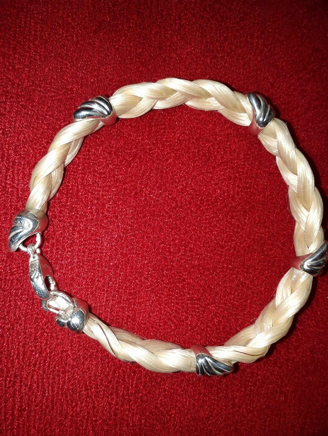 Bracelet tressé couleur crème avec des fils argentés sur fond rouge