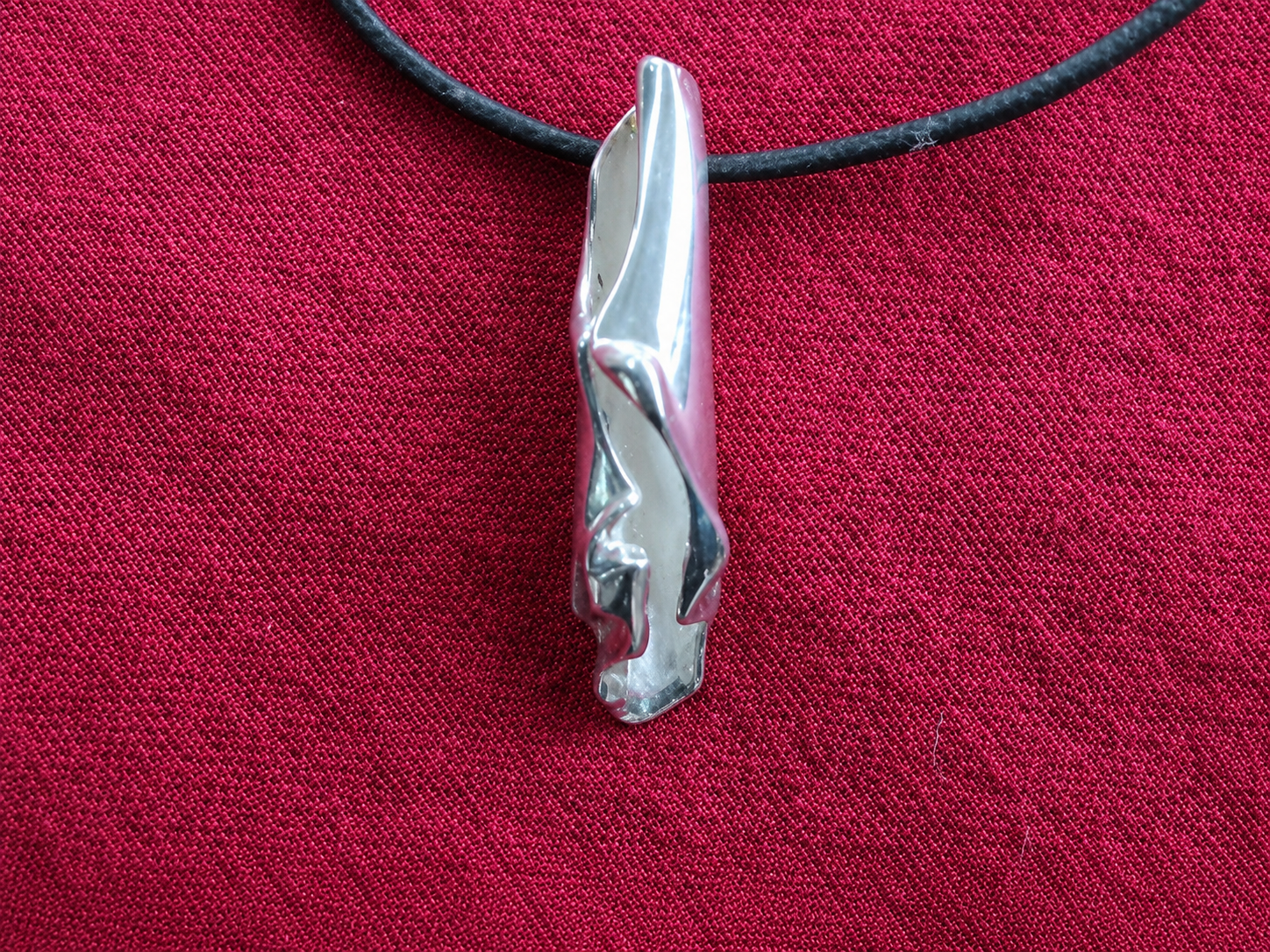 Pendentif en argent sur un cordon noir, sur fond de tissu rouge