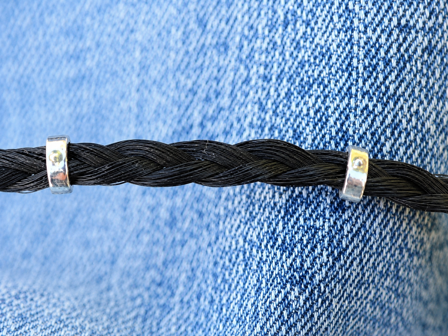 Cordon noir tressé maintenu par deux petites pinces argentées sur un tissu en jean bleu.