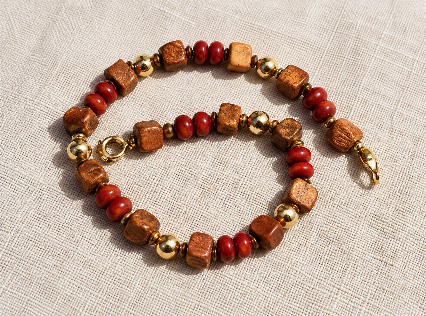 Deux bracelets de perles rouges, dorées et marron sur un fond en tissu beige