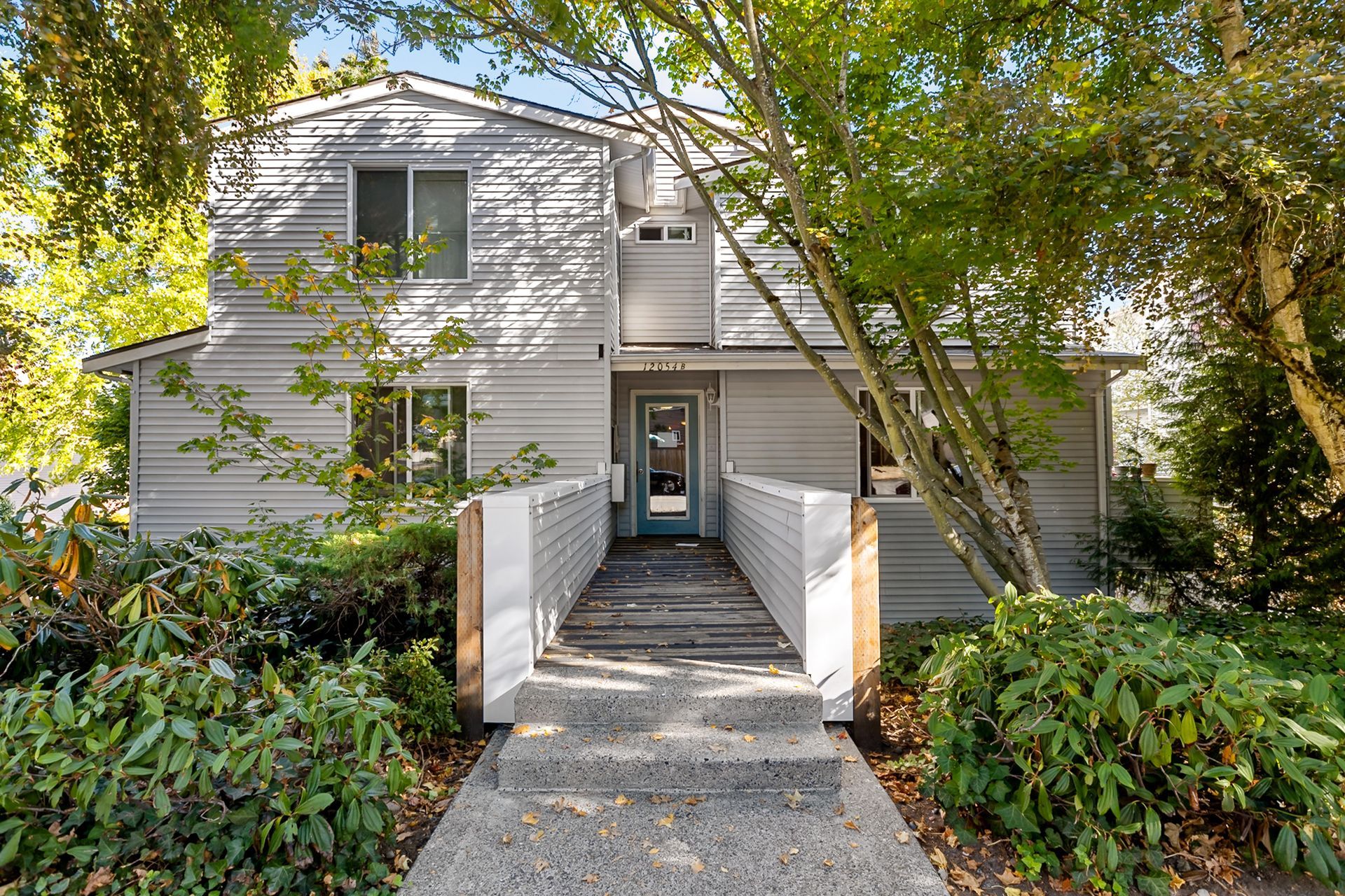 Walkway leading to a white two-story house surrounded by trees and shrubs