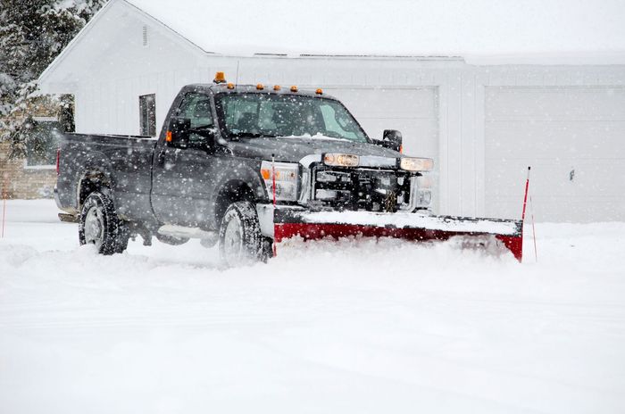A truck is plowing snow in front of a garage.