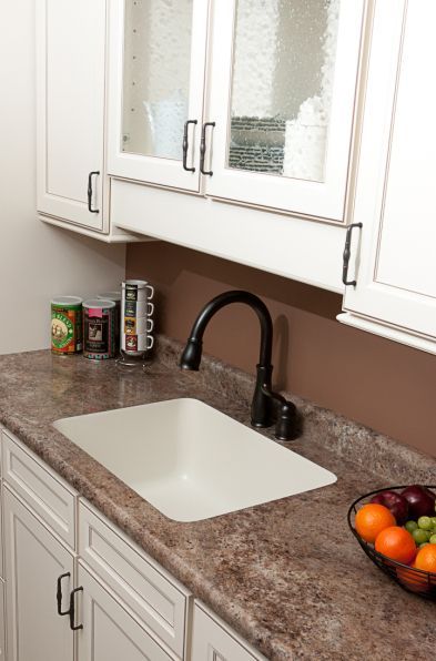 A kitchen with a sink and a bowl of fruit on the counter.