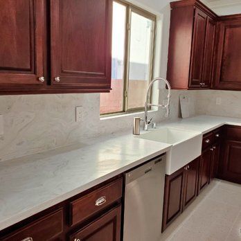 A kitchen with wooden cabinets , a sink , a dishwasher and a window.