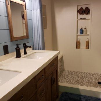 A bathroom with two sinks , a mirror , and a walk in shower.