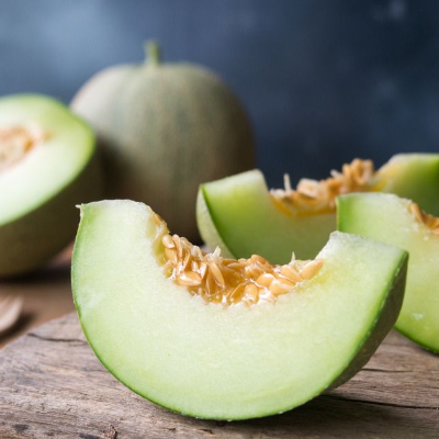 Gesneden groene meloen met pitjes, een hele meloen op de achtergrond, op een houten ondergrond.