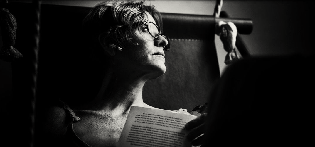 Zwart-witportret van iemand die een boek leest, verlicht door een raam in een donkere kamer